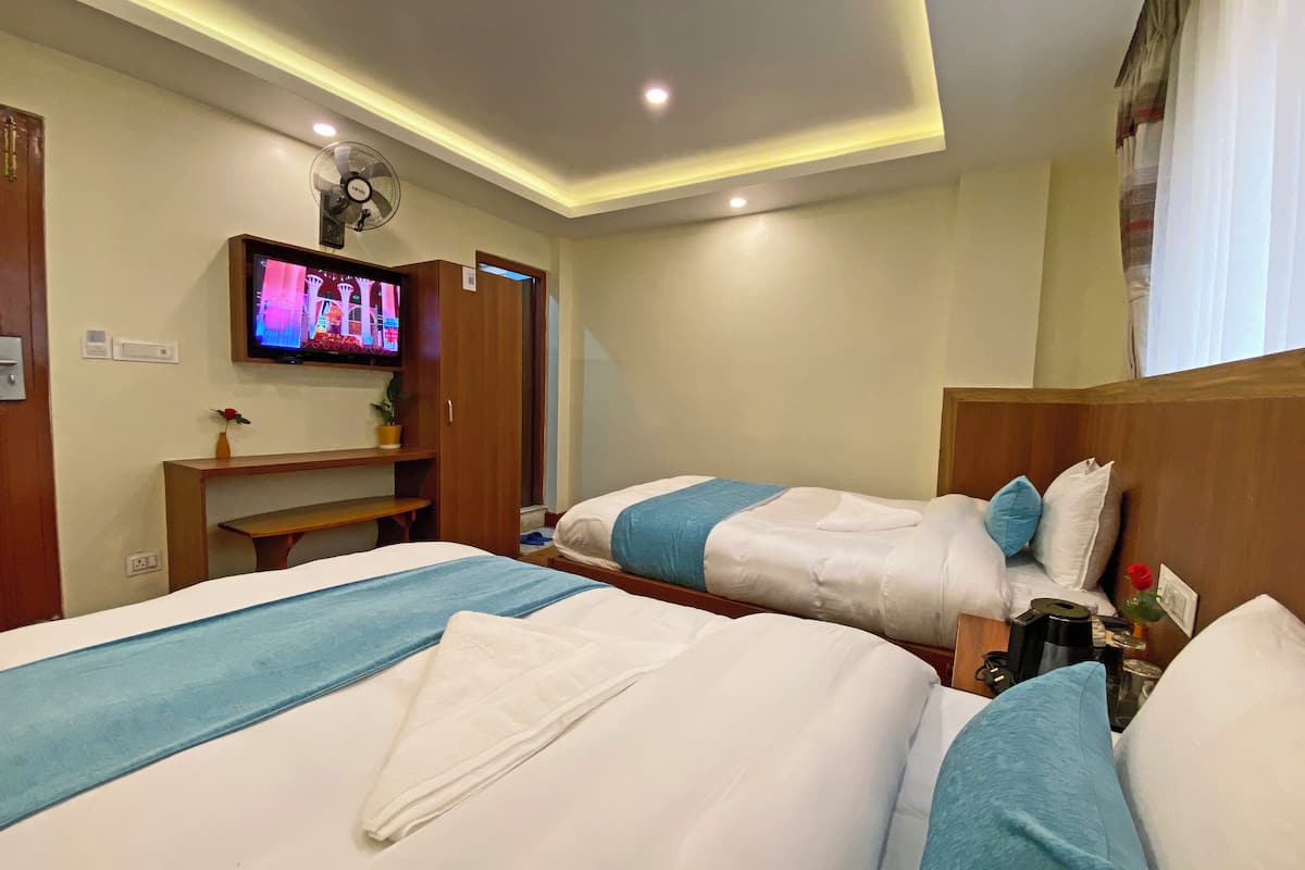 A hotel room with two beds, a TV, a desk, and a fan.