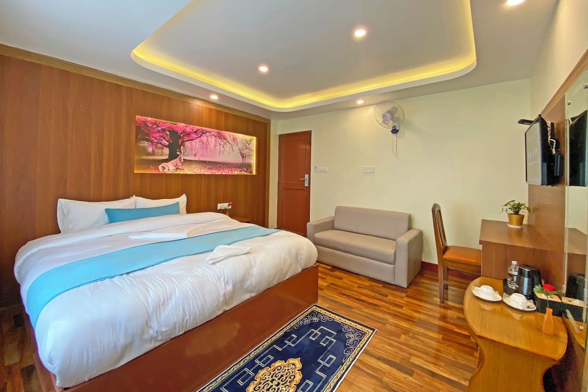 A hotel room with a large bed, a sofa, a small table with a plant, and a ceiling fan.