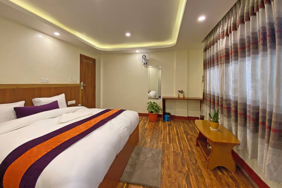 A hotel room with a large bed, a wooden floor, a desk, and a mirror.