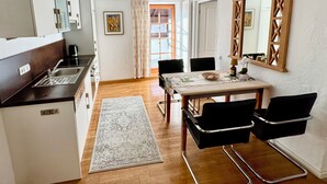 Et kompakt køkken med moderne hårde hvidevarer, et spiseområde med bord og stole, og et stort spejl på væggen.