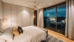 A modern bedroom with a large bed, a ceiling fan, and a view of a cityscape through a large window.