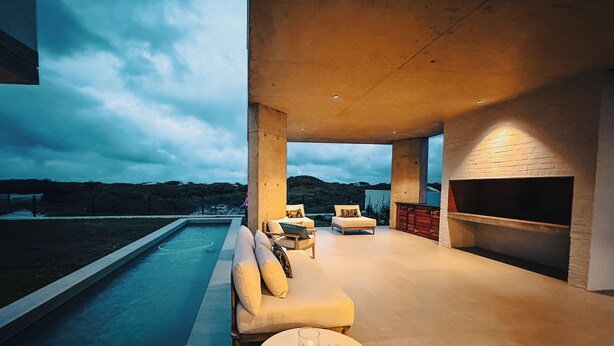 A modern outdoor living area with a pool, seating, and a fireplace.