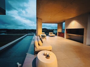 A modern outdoor living area with a pool, seating, and a fireplace.