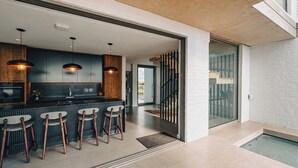 A modern kitchen with bar stools, pendant lighting, and a view to a balcony.