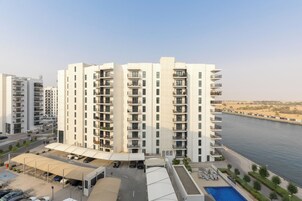 Un edificio residencial de varios pisos con balcones, zona de estacionamiento techada y una piscina.