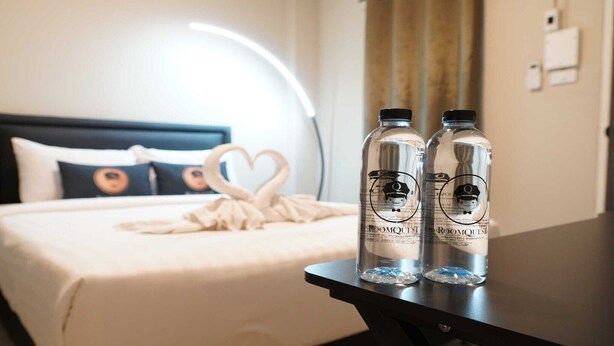 Una cama bien hecha con una toalla con forma de corazón y dos botellas de agua sobre una mesita de noche.