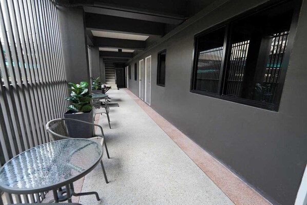 A corridor with metal chairs and tables, a plant, and a window with bars.