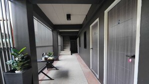 Un couloir avec un escalier menant à un palier, une porte portant un numéro et des plantes en pot.