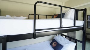 Un lit superposé avec une literie et des oreillers blancs, une structure en métal et une petite table sur laquelle se trouvent une tasse et une soucoupe.