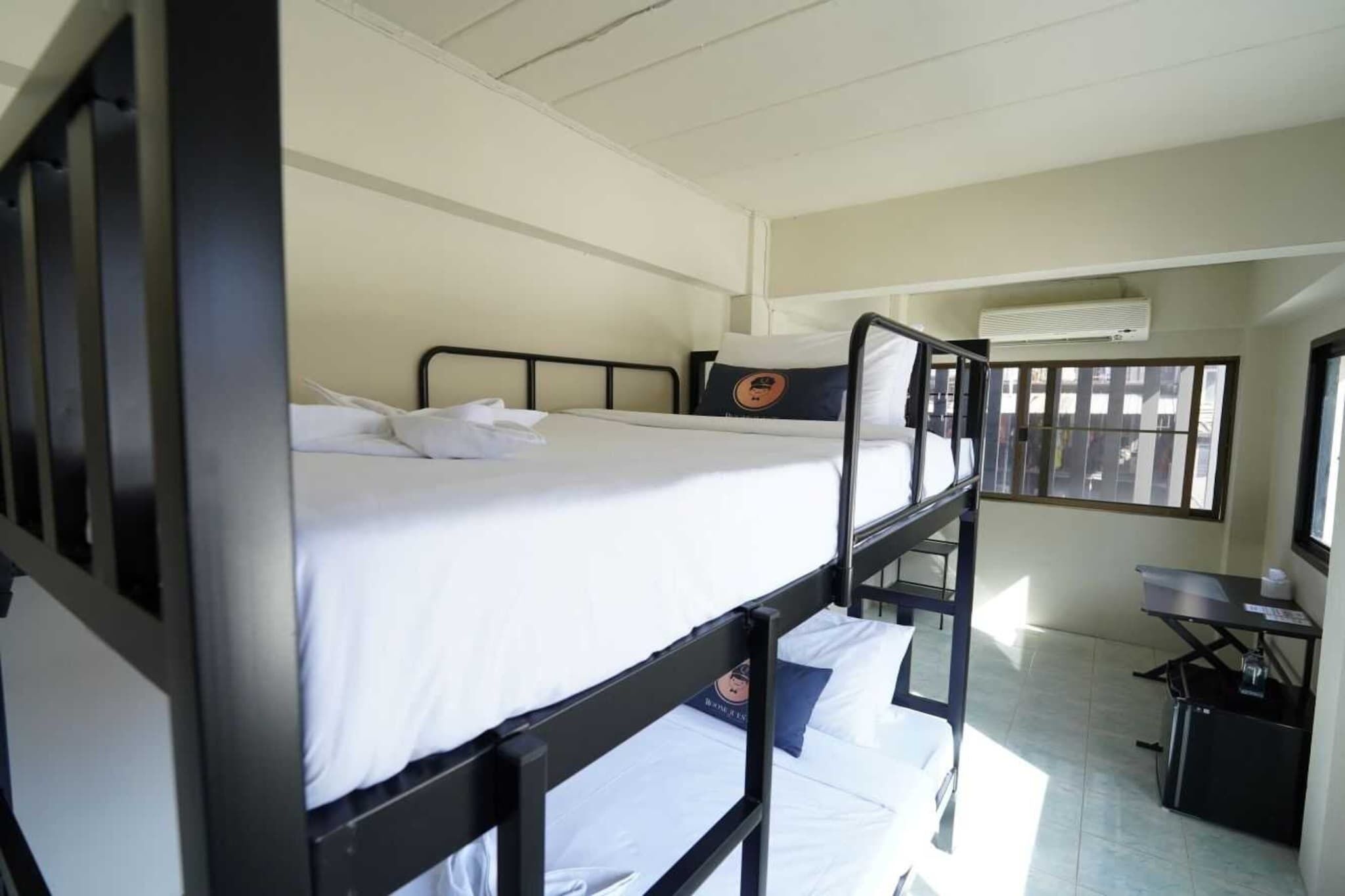 Een kamer met een stapelbed, een bureau en een stoel, een raam met zonwering en een airconditioningunit aan de muur.