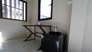 Une petite cuisine équipée d’un réfrigérateur noir, d’une petite table et d’une fenêtre laissant entrer la lumière naturelle.