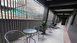 Un couloir avec des garde-corps en métal, un espace détente avec des chaises et une table, et des plantes en pot.