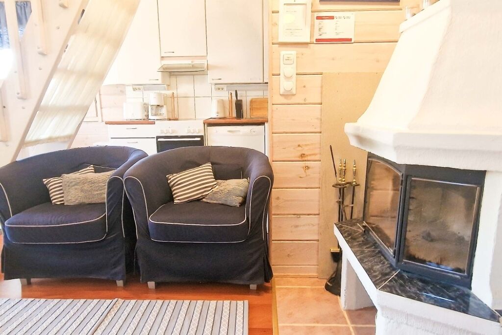 A cozy room with two dark armchairs, a fireplace, and a kitchen area in the background.