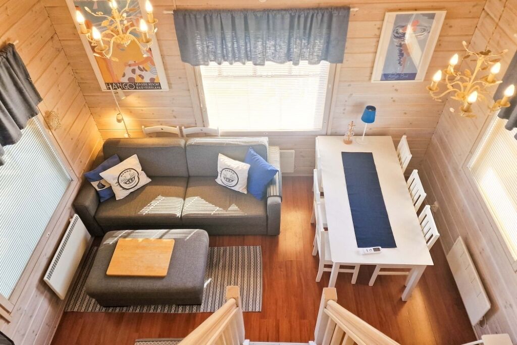 Un intérieur de chalet chaleureux avec un canapé, un pouf, une table à manger et deux lustres.