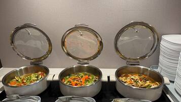 Drie buffettafels met voedselcontainers en bestek.