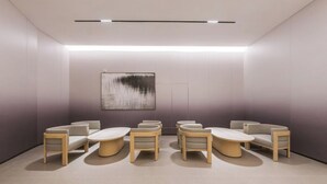 A modern waiting area with a minimalist design, featuring a row of cushioned chairs and a central table, with a large abstract painting on the wall. - Full Season Hotel-HGH (Hangzhou)