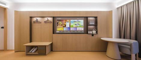 Habitación de hotel moderna con pared de paneles de madera, pantalla digital que muestra información de la habitación, una mesita y una zona de estar.