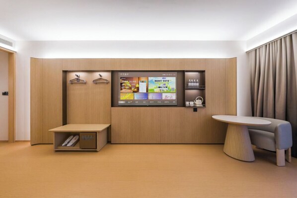 Habitación de hotel moderna con pared de paneles de madera, pantalla digital que muestra información de la habitación, una mesita y una zona de estar.