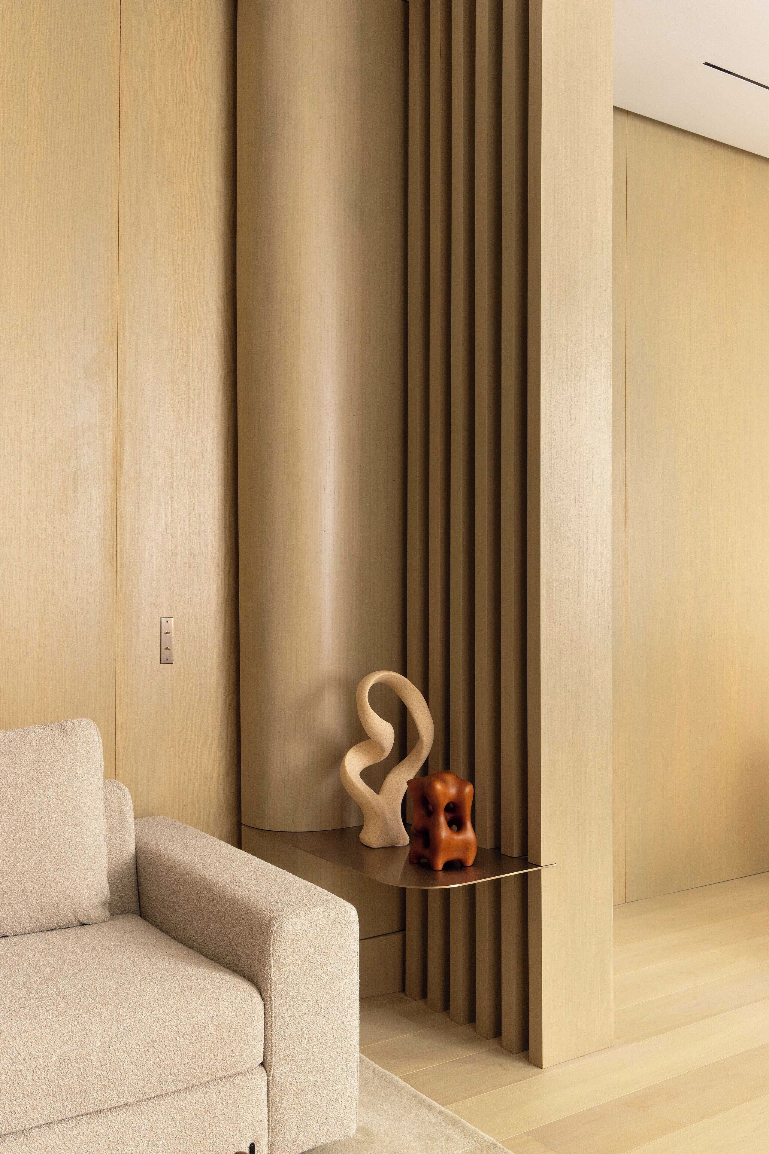 A modern interior with a sofa, a wooden sculpture, and a vertical panel wall.
