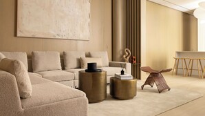 Ein modernes Wohnzimmer mit einer Eckcouch, zwei runden Gold-Beistelltischen, einem einzigartigen gewobenen Sessel und einem großen abstrakten Gemälde an der Wand.