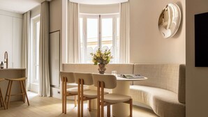 Ein modernes Wohnzimmer mit einem runden Tisch, vier Stühlen, einer Couch und einem großen Fenster mit Vorhängen.