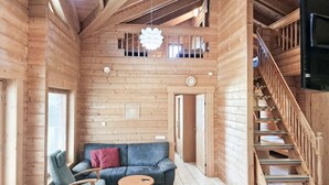 A wooden cabin interior with a sofa, chairs, a table, a staircase, and a hanging light fixture. - Villa Persikka, Himoslaakso Ski-in/out (Keski-Suomi)