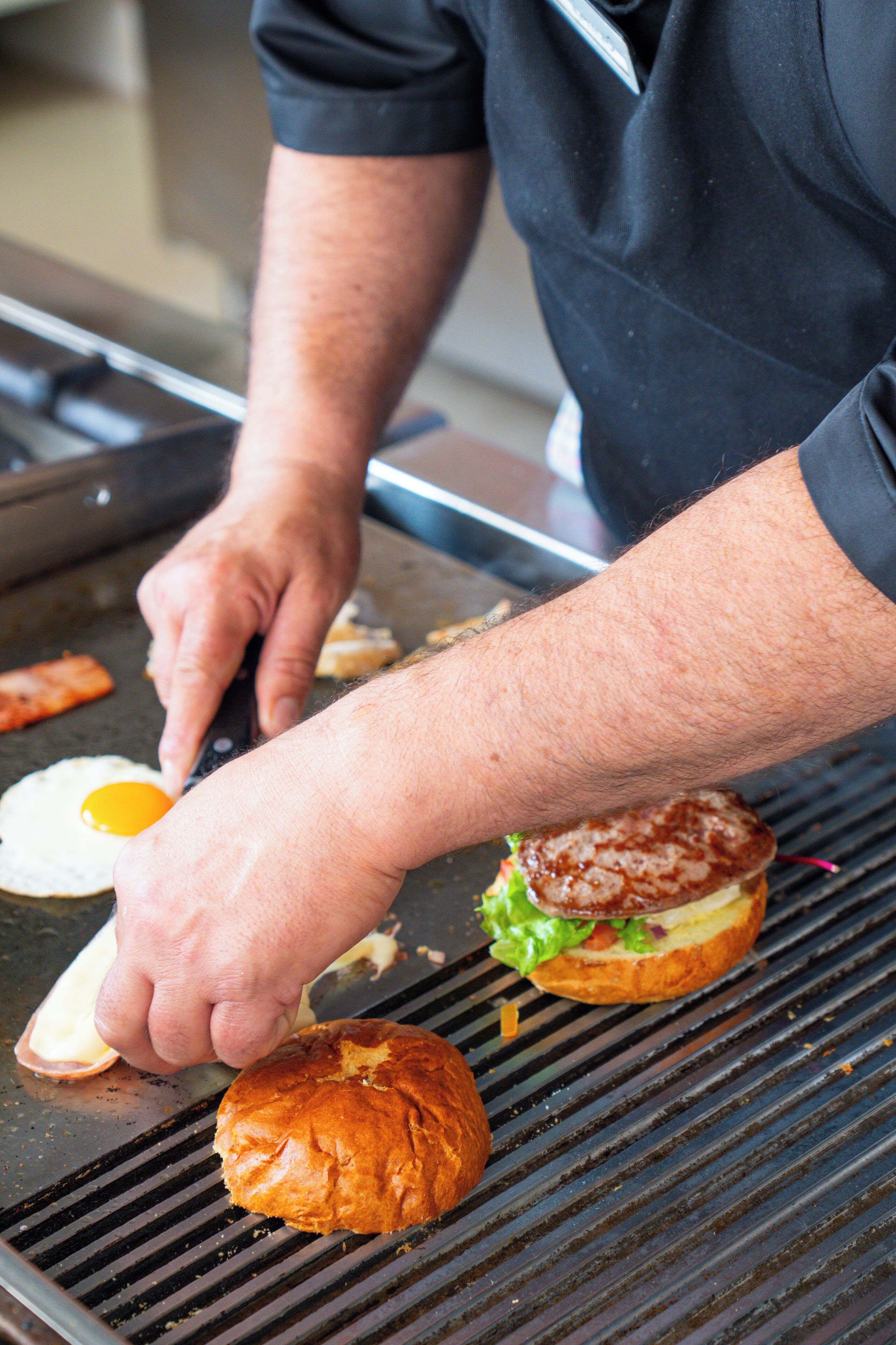 A person cooking a burger and an egg on a grill.