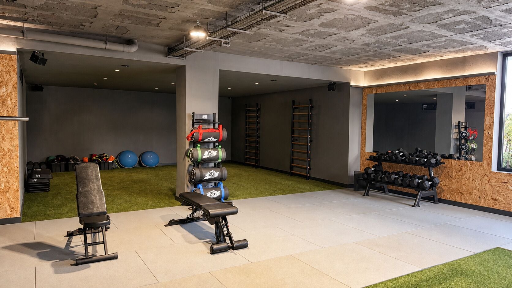 Ein Fitnessraum mit Kraftgeräten, einer Bank und einem an der Wand befestigten Hantelständer.