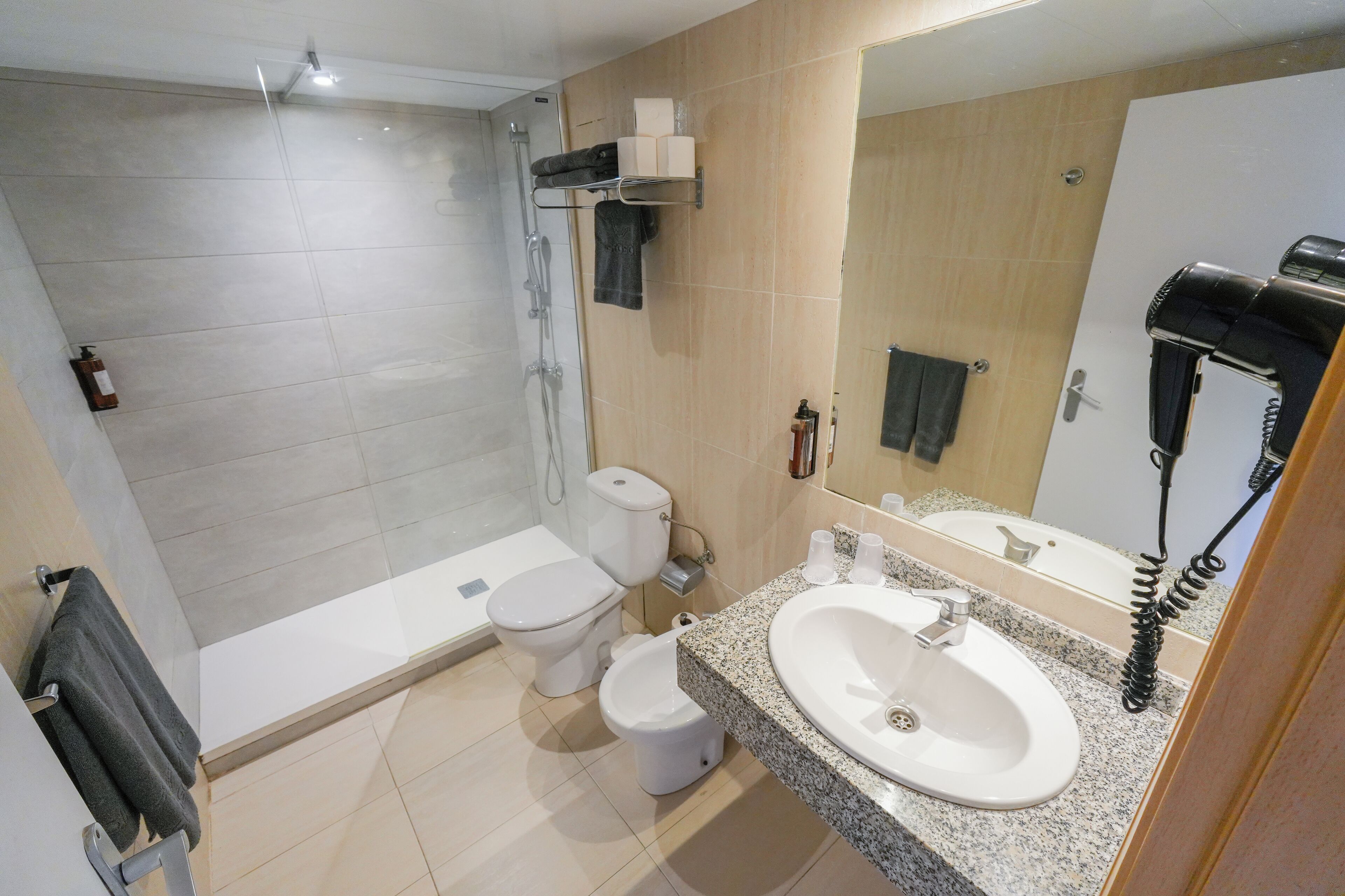A modern bathroom with a shower, toilet, bidet, and a sink with a hairdryer.