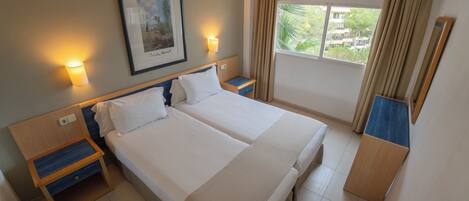A hotel room with two beds, a nightstand, a framed picture, a window with curtains, and a mirror.