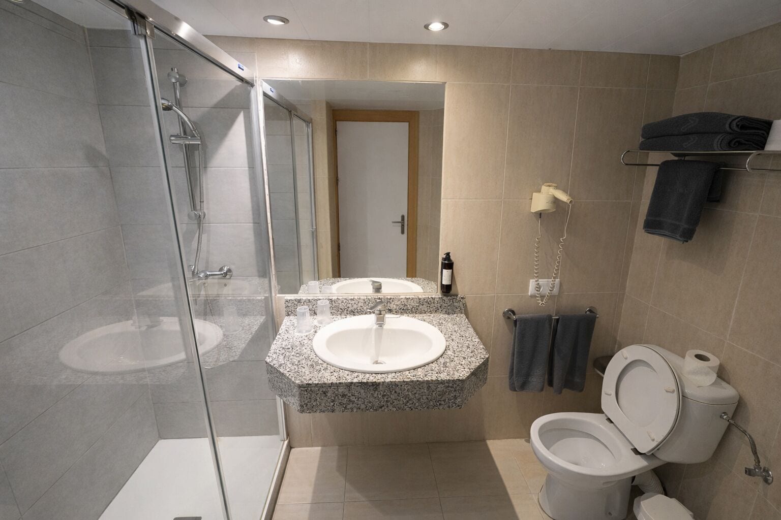 A modern bathroom with a glass shower enclosure, a granite sink, a toilet, and a towel rack.