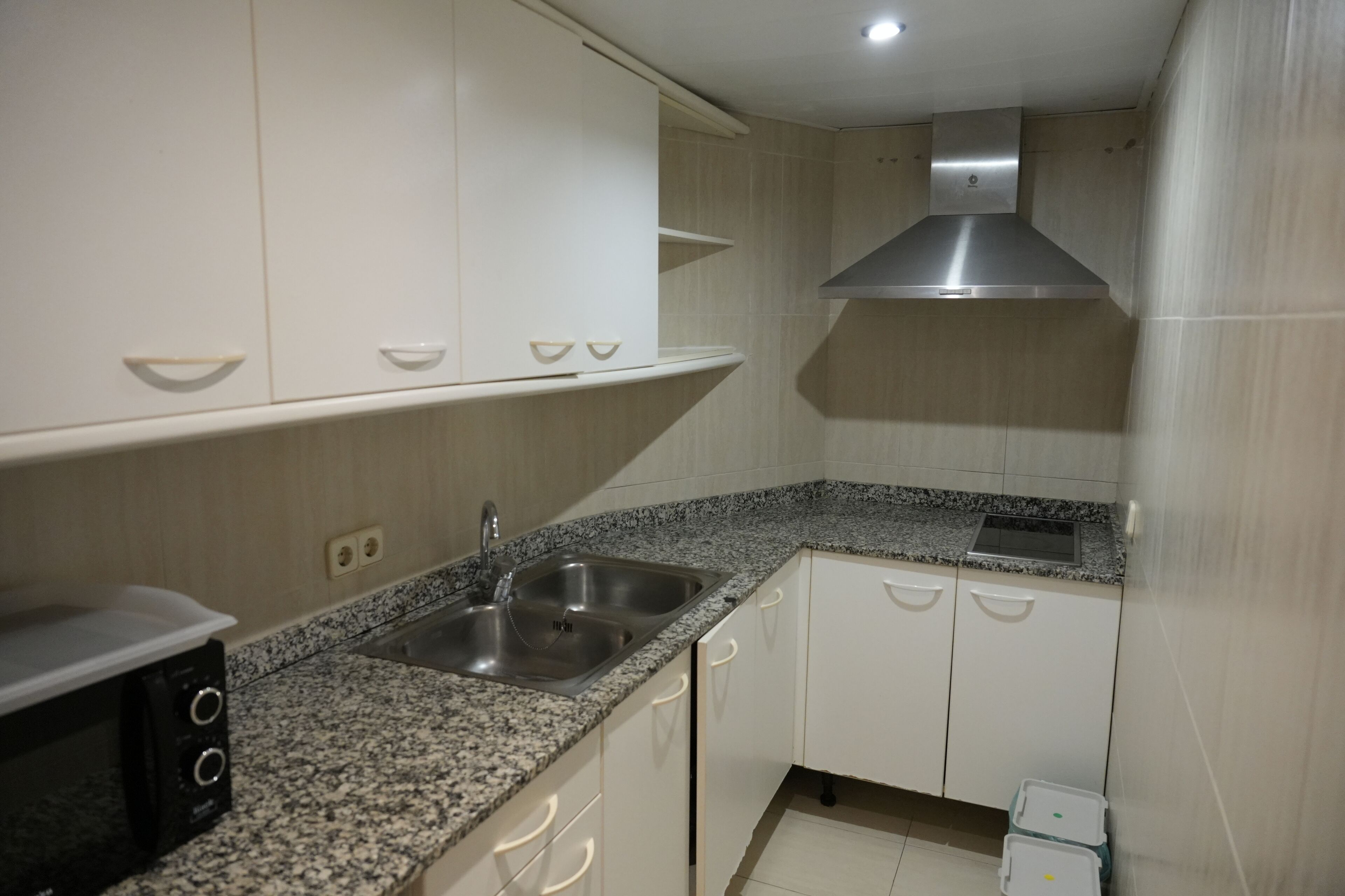 Cozinha compacta com armários brancos, bancada de granito, pia de aço inoxidável e coifa.