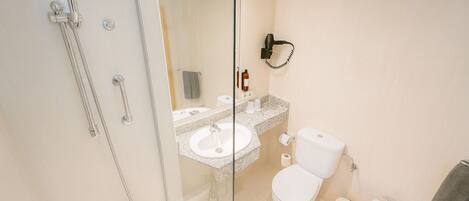 A modern bathroom with a glass-enclosed shower, a sink, toilet, bidet, and a hairdryer mounted on the wall.