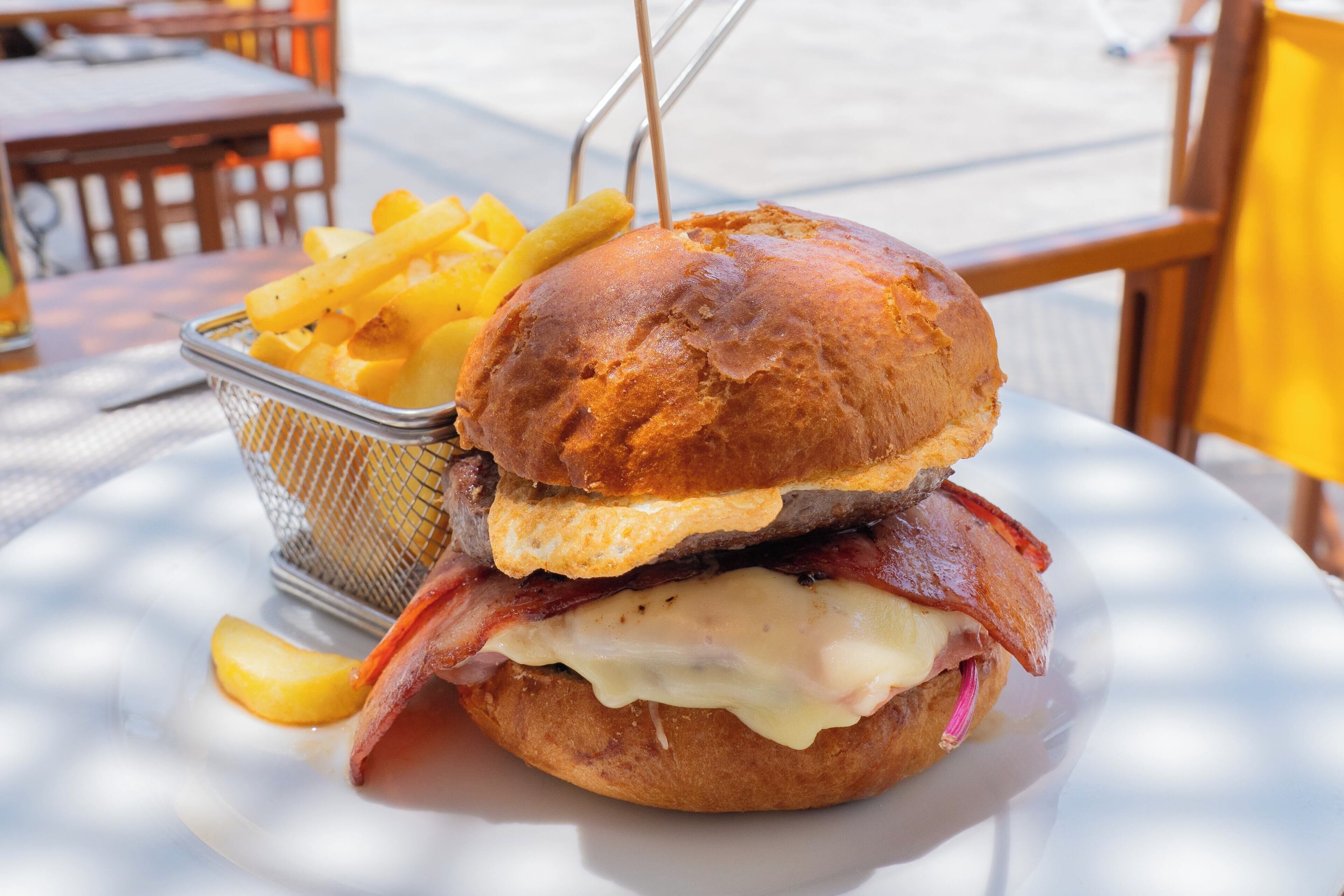 Un sándwich de tocino, queso y huevo frito en un pan, acompañado de una porción de papas fritas sobre un plato blanco.