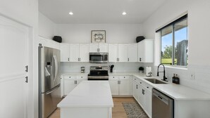 A modern kitchen with white cabinetry, stainless steel appliances, and a large island.
