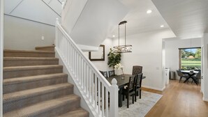 A modern interior with a staircase, dining area, and a view of the outdoors.