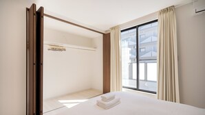 Et hotelværelse med en stor seng, en skydedør, et vindue med gardiner og udsigt til en bygning.