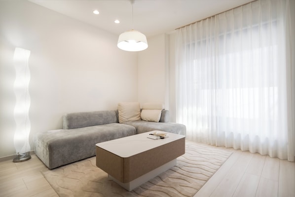 Ein modernes Wohnzimmer mit einem grauen Sofa, einem weißen Couchtisch und transparenten weißen Vorhängen.