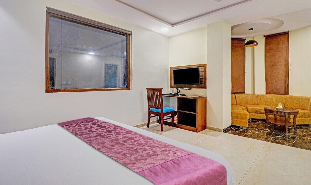 A hotel room with a bed, a desk with a computer, a TV, a sofa, and a small table.