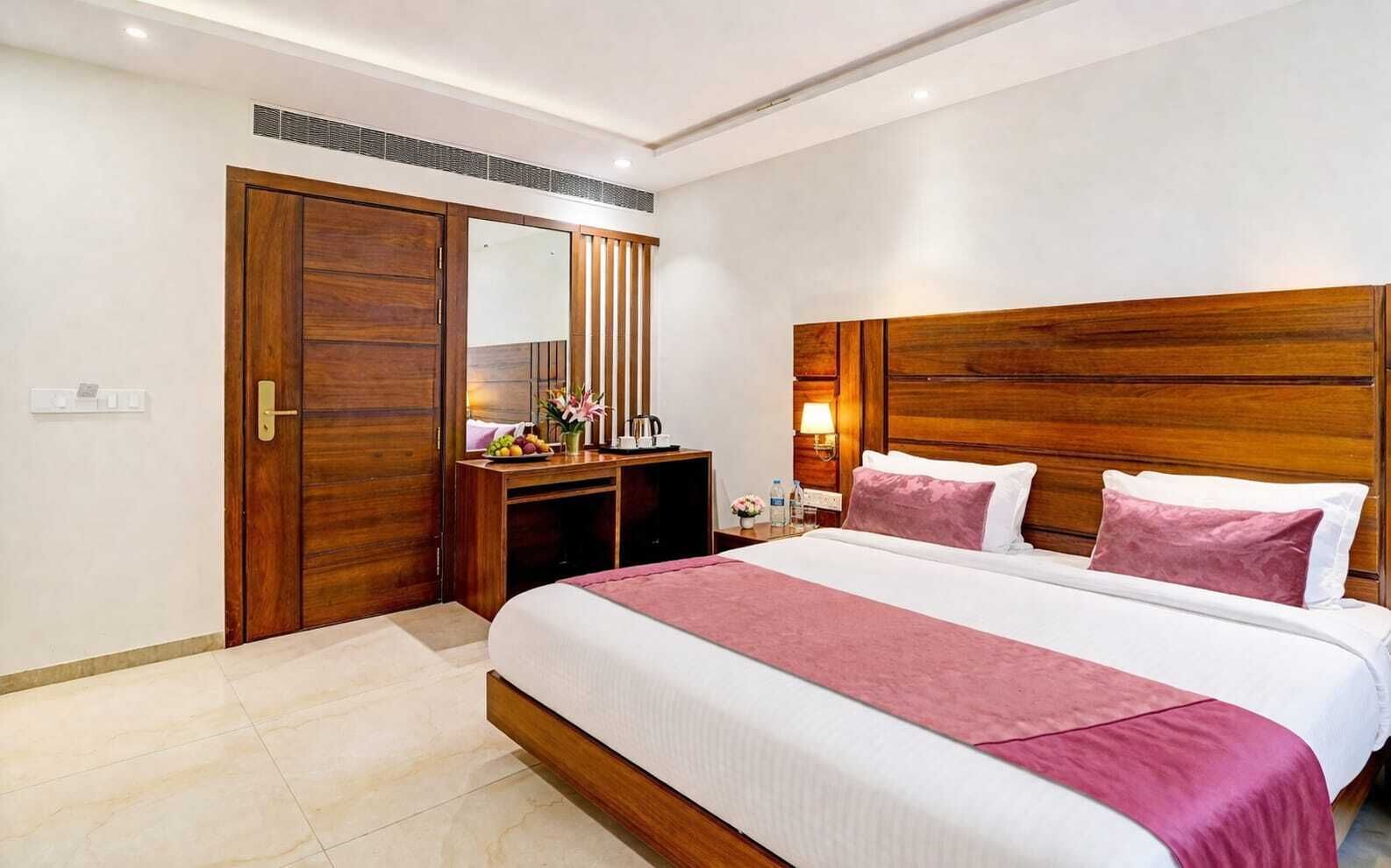 A hotel room with a large bed, a wooden wardrobe, a desk with a mirror, and a nightstand with a lamp.
