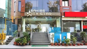 Het uiterlijk van Hotel Sahibs City Star met een glazen gevel, een trap naar de ingang en potplanten rondom het entreegebied.
