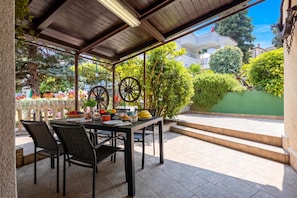 A covered outdoor dining area with a table set for two, surrounded by chairs. - Beach House Astrid Malinska (Malinska-Dubasnica)