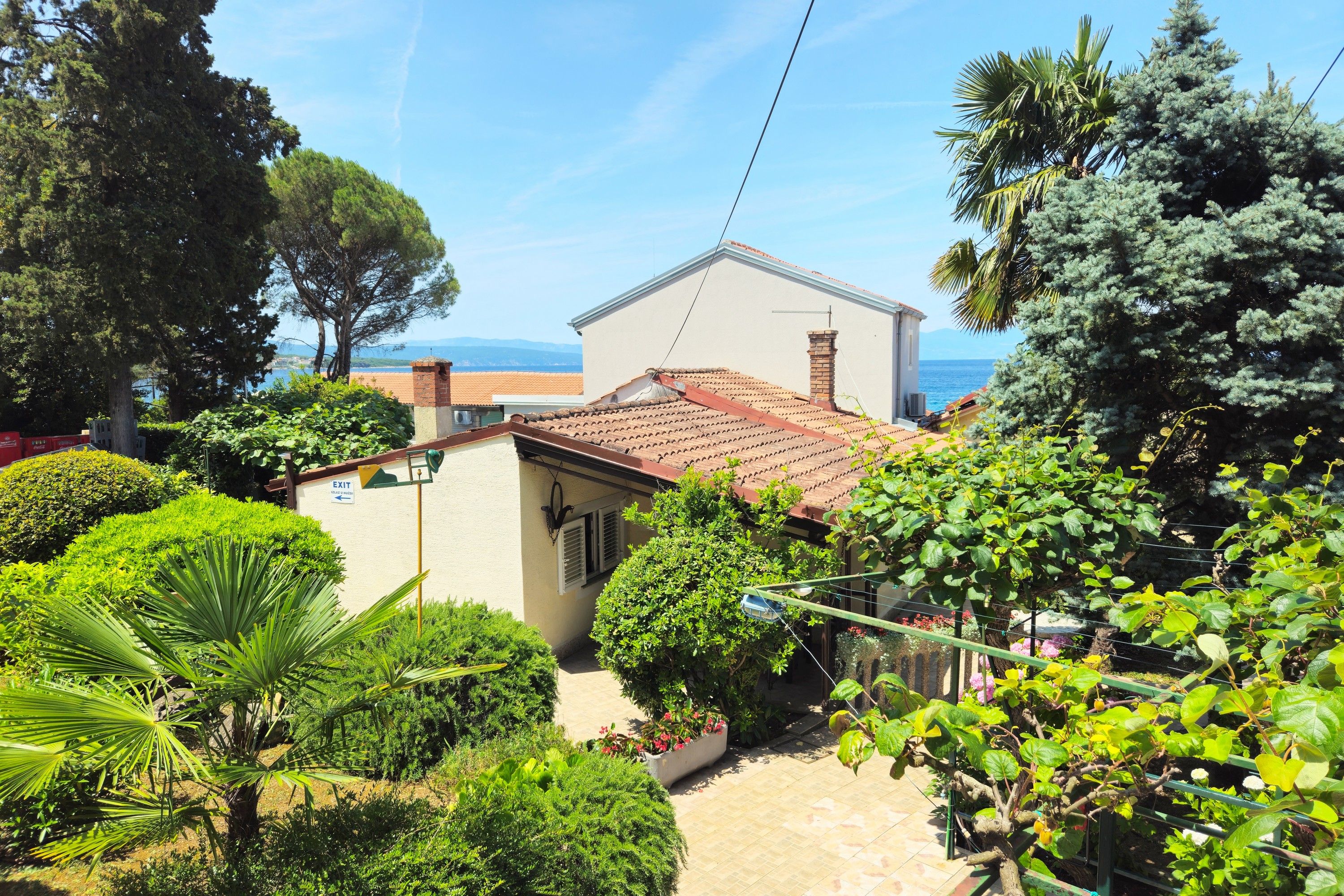 A residential property with a tiled roof, a small garden with various plants, and a view of the sea.