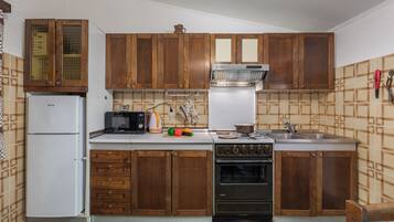 A compact kitchen with wooden cabinets, a white refrigerator, a microwave, and a stove.