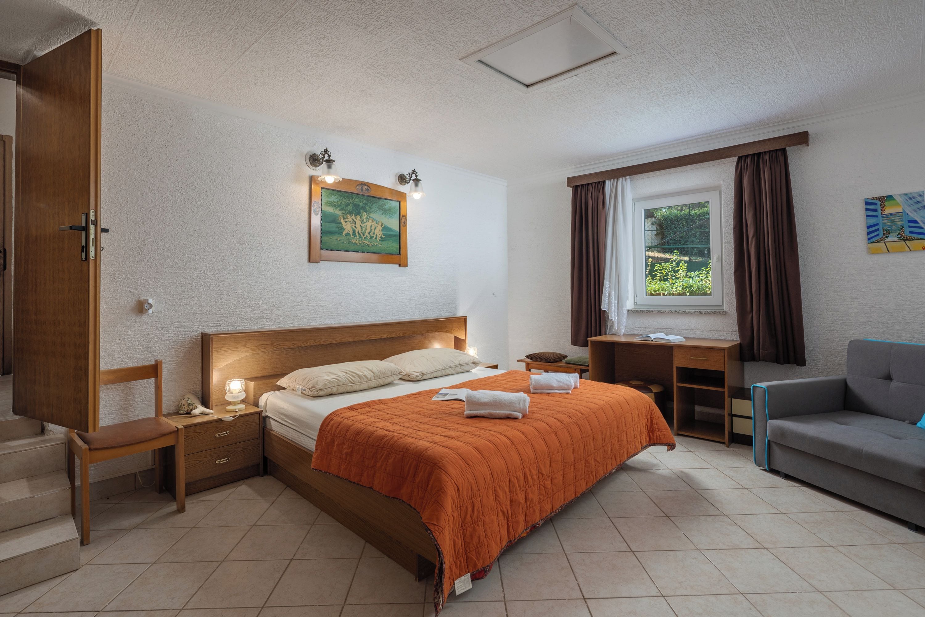 Une chambre à coucher comprenant un lit, des tables de chevet, un bureau, une chaise, une fenêtre avec des rideaux et un tableau accroché au mur.