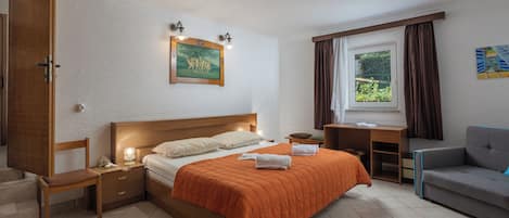 A bedroom with a bed, bedside tables, a desk, a chair, a window with curtains, and a painting on the wall.