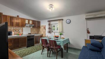 A compact kitchen with wooden cabinets, a dining table with chairs, a sofa, and a television.