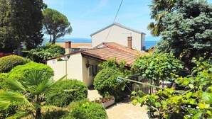 A residential property with a tiled roof, a small garden with various plants, and a view of the sea. - Beach House Astrid Malinska (Malinska-Dubasnica)