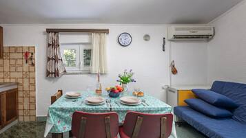 Un comedor con una mesa preparada para dos personas, un reloj en la pared y un sofá azul al fondo.
