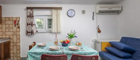 A dining area with a table set for two, a clock on the wall, and a blue sofa in the background.